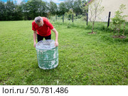 Pulling plastic liner over rim of weathered water butt standing on grassy garden lawn with open space and clear sky in background. Стоковое фото, фотограф Владимир Григорьев / Фотобанк Лори