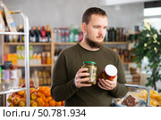 Man carefully selects canned tomatoes and cucumbers in the produce section of supermarket. Стоковое фото, фотограф Яков Филимонов / Фотобанк Лори