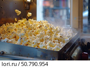 Popcorn machine popping delicious kernels into a metal tray. Стоковое AI-изображение, AI-художник Иван Рябоконь / Фотобанк Лори
