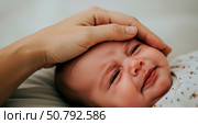 Woman gently strokes a crying baby. Close up of a newborn with teary eyes. Concept of parental care, comfort, and soothing a child. Стоковое AI-изображение, AI-художник Анжелика Самсонова / Фотобанк Лори