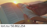Hands hold open Bible book and wooden cross at beach during glowing sunset. Стоковое видео, видеограф Igor Tichonow / Фотобанк Лори