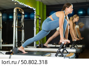 Young woman standing on pilates reformer, perform exercises. Стоковое фото, фотограф Яков Филимонов / Фотобанк Лори