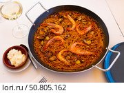 Fideua marinera(Spanish) seafood noodles with shrimps and mussels served in a pan with a glass of wine and sauce in the restaurant. Стоковое фото, фотограф Яков Филимонов / Фотобанк Лори