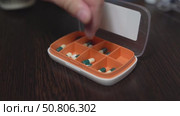Hand placing light-yellow vitamin D capsules into a weekly pill organizer for medication management. Стоковое видео, видеограф Татьяна Степанищева / Фотобанк Лори