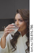 Attractive young Latin woman, with long black hair, drinking glass of clean, cold water while wearing white robe. Стоковое видео, видеограф Strunov David / Фотобанк Лори