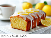Homemade lemon drizzle cake with icing. Classic lemon pound cake with citrus glaze and zest. Whole loaf, side view, close up. Fresh homemade baked dessert with lemon slices. Blurred tea set background. Стоковое AI-изображение, AI-художник Марина Демидюк / Фотобанк Лори