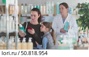Selective middle-aged woman with daughter scanning barcode on mouthwash liquid, pharmacist consulting her in chemistry. Стоковое видео, видеограф Яков Филимонов / Фотобанк Лори