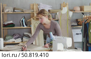 Woman tailor cuts fabric with tailor's scissors on the table. Seamstress works in a workshop and prepares fabric for sewing. Стоковое видео, видеограф Яков Филимонов / Фотобанк Лори