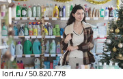 Young Spanish woman chooses household chemicals in a supermarket decorated for Christmas. Girl in a coat came to the hardware store on New Year's Eve. Стоковое видео, видеограф Яков Филимонов / Фотобанк Лори