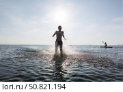 Мальчик бежит по воде в солнечный день, фигура с веслом плывёт на заднем плане. Стоковое фото, фотограф Мария L. / Фотобанк Лори