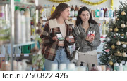 Women buy nail polishes and a set of makeup cosmetics against the background of a Christmas tree in the supermarket. Customers choose a set of cosmetics for festive New Year promotions and discounts. Стоковое видео, видеограф Яков Филимонов / Фотобанк Лори