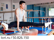 Male athlete doing complicated exciting trick on pommel horse in professional gym. Стоковое фото, фотограф Татьяна Яцевич / Фотобанк Лори
