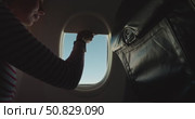 Passenger in striped shirt opens airplane window shade, letting sunlight fill the aircraft cabin, view of clear blue sky through porthole, travel moment with seatback, tray table and paper cup. Стоковое видео, видеограф Сергей Тимофеев / Фотобанк Лори