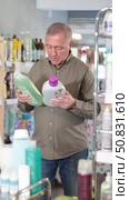 Elderly European man in the household section of a supermarket holds rinses and fabric softeners. Buyer chooses a liquid laundry detergent. Стоковое видео, видеограф Яков Филимонов / Фотобанк Лори