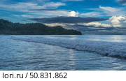 Morning by the ocean. The waves are foaming and spreading. A hill in the distance. The clouds in the blue sky are illuminated with golden light. Malaysia. Borneo. Kota Kinabalu. Стоковое фото, фотограф Вера Ивановна Кубарева / Фотобанк Лори
