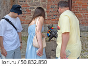 Люди рассматривают и держат за лапку бронзовую скульптуру кота Филимона на территории Выборгского замка в городе Выборге Ленинградской области. Редакционное фото, фотограф Румянцева Наталия / Фотобанк Лори