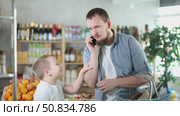 Dad and son, while shopping for groceries, call up with mom, discuss on phone purchase of snacks. Стоковое видео, видеограф Яков Филимонов / Фотобанк Лори