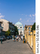 Yevpatoria, Russian Federation - July 05, 2025: Street view of bustling city with historic architecture and blue domed church under clear sky, showcasing vibrant urban life and cultural heritage. Редакционное фото, фотограф Ирина Ручушкина / Фотобанк Лори