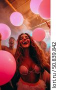 Party celebration: Upward angle of laughing woman amidst pink balloons and jubilant friends, capturing youthful exuberance. Стоковое AI-изображение, AI-художник Данила Большаков / Фотобанк Лори
