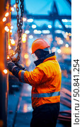 Night Shift: Industrial Worker Securing Chains in Rainy Conditions. Стоковое AI-изображение, AI-художник Данила Большаков / Фотобанк Лори