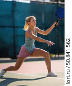 Young female athlete lunges to return shot during active pickleball game, showing agility, competitive energy, and outdoor sports dedication. Стоковое AI-изображение, AI-художник Александра Троицкая / Фотобанк Лори