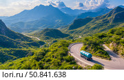 Scenic transport: water tanker descends winding mountain road amidst lush green vegetation. Стоковое AI-изображение, AI-художник Данила Большаков / Фотобанк Лори