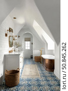 Elegant attic bathroom with white tiles, gold fixtures, copper bathtub, and patterned blue floor tiles. Стоковое AI-изображение, AI-художник Катерина Бондарец / Фотобанк Лори