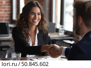 Smiling businesswoman in a black blazer confidently shakes hands with a man across a desk in a modern office, symbolizing successful negotiation or job interview. Стоковое AI-изображение, AI-художник Катерина Бондарец / Фотобанк Лори