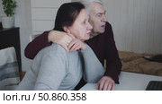 Senior couple using laptop together in the room. Embracing elderly man and woman reading email or online shopping choice. Old man and woman talk at table in home together on internet, social media. 4K. Стоковое видео, видеограф Марина Демидюк / Фотобанк Лори