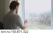 Man is cleaning window in apartment. Adult Male cleaner using a squeegee to wash a window. Bearded guy wiping and washing glasses with with spray bottle, rag and vacoom. Everyday chores. Purification. Стоковое видео, видеограф Марина Демидюк / Фотобанк Лори