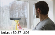 Man is cleaning window in apartment. Adult Male cleaner using a squeegee to wash a window. Bearded guy wiping and washing glasses with with spray bottle, rag and vacoom. Everyday chores. Purification. Стоковое видео, видеограф Марина Демидюк / Фотобанк Лори