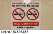 Знаки и надписи на русском и английском языках. Курение запрещено. Предусмотрен штраф. Правила нахождения в помещении. Забота о здоровье посетителей. Табличка на стене туалета. Крупный план. Signs and inscriptions in Russian and English. No smoking. No vaping. A fine is applied. Indoor rules. Taking care of health of visitors. Sign on the toilet wall. Close-up. Стоковое фото, фотограф Ирина / Фотобанк Лори