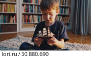 Preschool boy sitting cross legged on patterned floor mat, clutching wooden toy boat and imagining maritime exploration through distant sea routes. Стоковое AI-видео, аниматор Данил Руденко / Фотобанк Лори