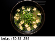 Miso soup with silken tofu, wakame seaweed, spring onions and sesame seeds in black bowl. Стоковое AI-изображение, AI-художник Иван Рябоконь / Фотобанк Лори