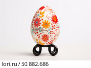 Decorated easter egg standing on a metal support on white background. Стоковое AI-изображение, AI-художник Иван Рябоконь / Фотобанк Лори
