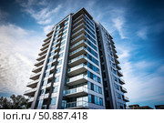 Modern residential skyscraper rising against blue sky with clouds. Стоковое AI-изображение, AI-художник Иван Рябоконь / Фотобанк Лори