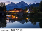 Watzmann reflecting in the river at night with illuminated bridge and houses. Стоковое AI-изображение, AI-художник Иван Рябоконь / Фотобанк Лори