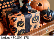 Halloween gift box wrapped with spooky orange and black paper and decorated with black ribbon. Стоковое AI-изображение, AI-художник Иван Рябоконь / Фотобанк Лори