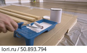 Preparation of paint roller for painting wooden planks, dipping roller in white paint tray. Pouring paint from can into tray close-up of tools, wood board protective film cardboard, renovation process. Стоковое видео, видеограф Сергей Тимофеев / Фотобанк Лори