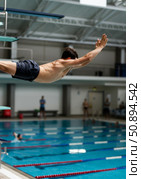 Diver performing a graceful springboard dive into a clear swimming pool with spectators in the background. Стоковое AI-изображение, AI-художник Гайфуллина Дина / Фотобанк Лори