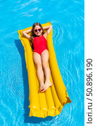 Top view little girl in red swimsuit lies comfortably on inflatable mattress in swimming pool with blue water on warm summer day on tropical vacation. Relaxation, fun, carefree childhood concept. Стоковое фото, фотограф Ирина Михайличенко / Фотобанк Лори