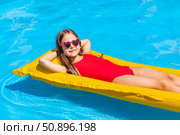 Little girl in red swimsuit lies on cozy inflatable mattress in swimming pool with blue water on warm summer day on tropical vacation. Relaxation, fun, carefree childhood concept. High quality photo. Стоковое фото, фотограф Ирина Михайличенко / Фотобанк Лори