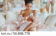 Graceful woman in lustrous satin attire, deeply absorbed by her modern handheld gadget on a comfortable large settee. Стоковое AI-видео, аниматор Данила Большаков / Фотобанк Лори
