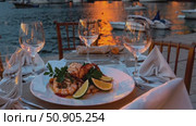 Romantic seaside dining featuring elegant seafood platter, crystal wine glasses, and candlelit table overlooking tranquil ocean waves at sunset. Стоковое AI-видео, аниматор Данил Руденко / Фотобанк Лори