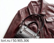 Maroon leather jacket with zippers and pockets and black leather stylish bag. Modern outerwear. Close-up. Fashion background. Autumn urban street clothes. Fashionable concept. Women's casual outfit. Стоковое AI-изображение, AI-художник Марина Демидюк / Фотобанк Лори