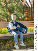 Little stylish schoolboy in blue bomber jacket sits on a bench with her backpack after school classes on sunny autumn day and looking at camera. Back to school concept. High quality photo. Стоковое фото, фотограф Ирина Михайличенко / Фотобанк Лори