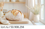 Artisan Bread Still Life: Rustic sourdough loaf on cutting board in a bright, naturally lit kitchen setting. Стоковое AI-изображение, AI-художник Данила Большаков / Фотобанк Лори