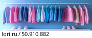 Clothing Rack Assortment: Display of pastel hoodies, denim jackets and sneakers on a pastel blue wall, suggesting a trendy and coordinated collection. Стоковое AI-изображение, AI-художник Данила Большаков / Фотобанк Лори