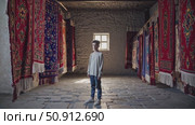 Young artisan stands proudly amidst a vibrant display of handcrafted carpets in a workshop, the rich colors and intricate patterns creating a captivating backdrop. Стоковое AI-видео, аниматор Данил Руденко / Фотобанк Лори