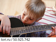 Handsome dad teaches his cute son to play the guitar sitting on sofa in the living room at home. Happy Father's Day. Father teaching his child to play guitar. Kid Learning music skill. Art education. Стоковое фото, фотограф Марина Демидюк / Фотобанк Лори